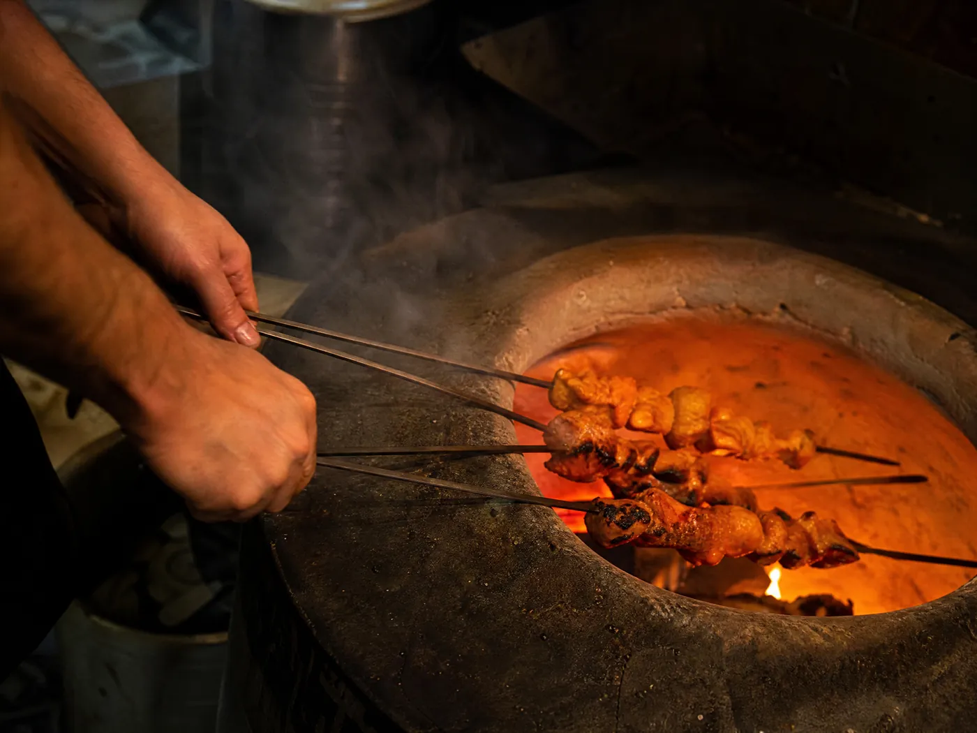 Skewers of chicken tikka going into a glowing clay oven.